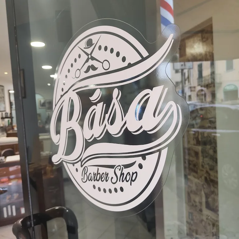 Il logo Bása dipinto sulla vetrina del negozio, accanto al palo da barbiere